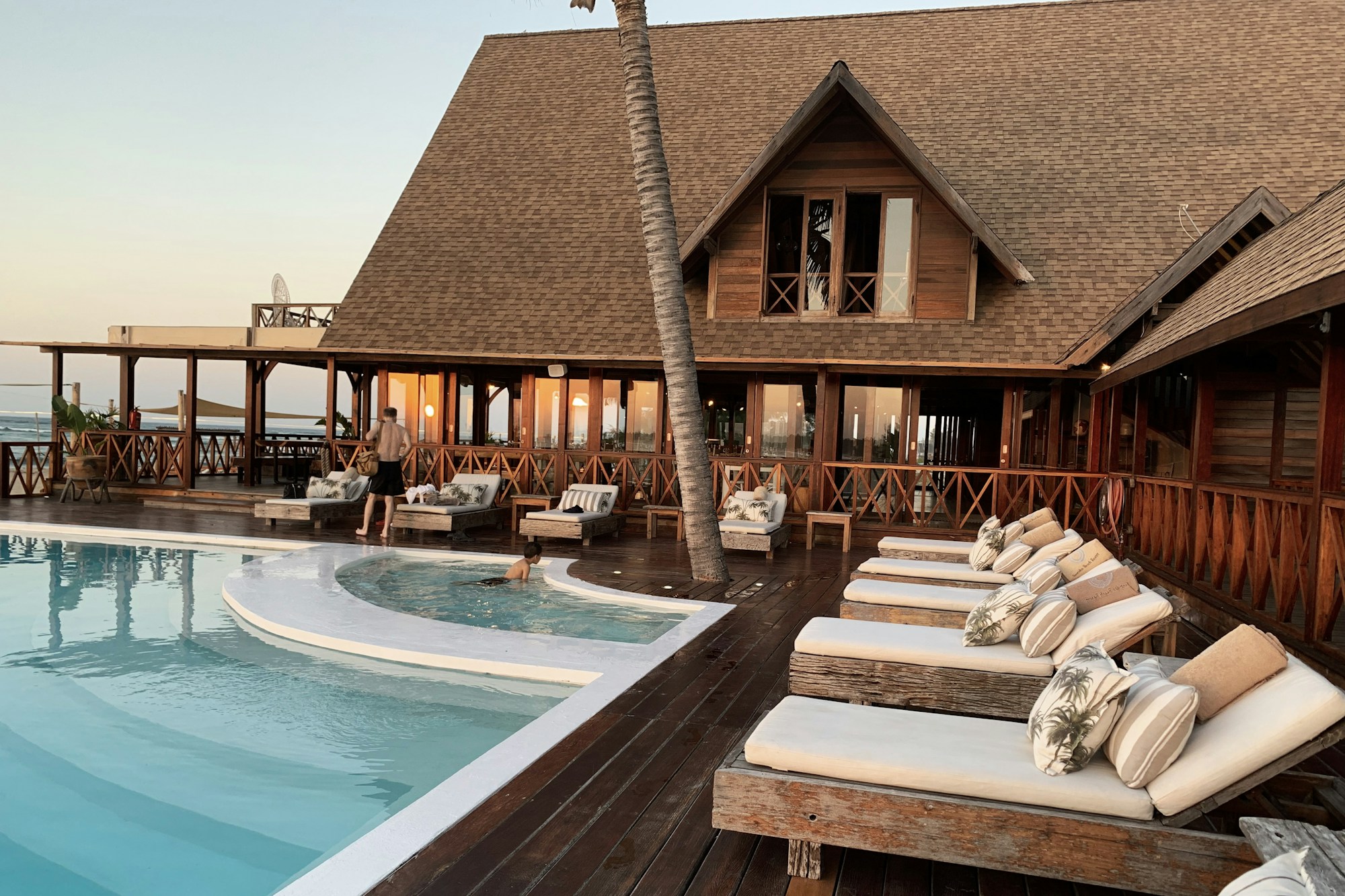 Resort swimming pool beside a timber-roofed hotel terrace and loungers